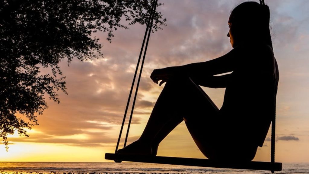 A person sitting on a swing at sunset, silhouetted against the sky.