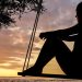 A person sitting on a swing at sunset, silhouetted against the sky.