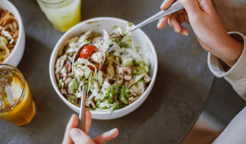 A person eating a fresh salad with a drink beside them.