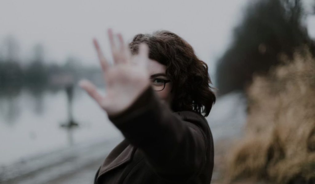 A person holding a hand up toward the camera, obscuring part of their face.