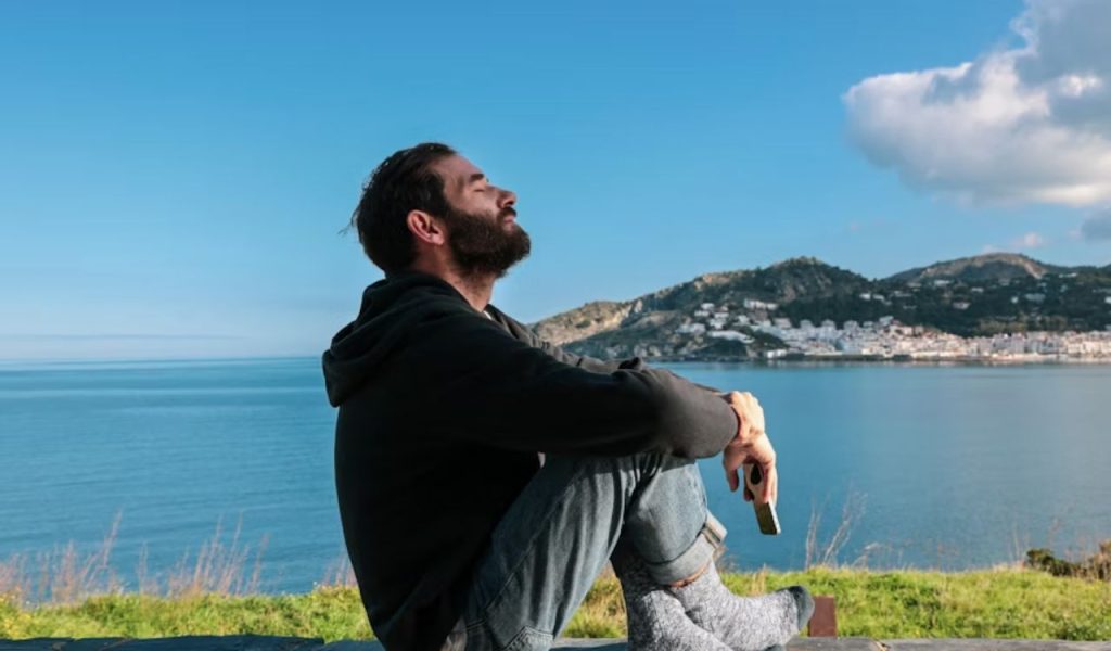 A person sitting by the water with eyes closed, enjoying the view.