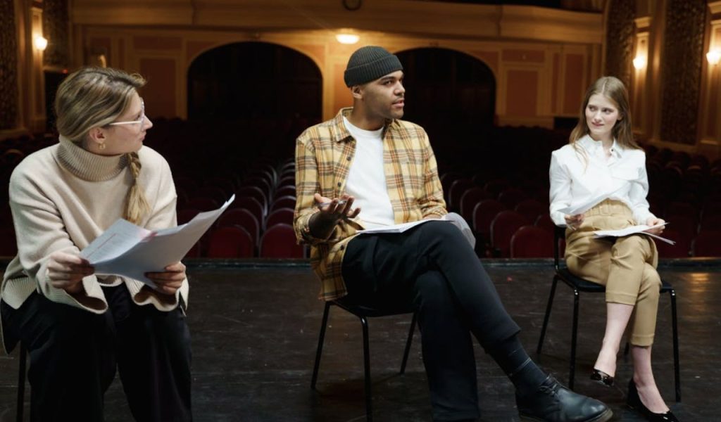 Three people sitting on a stage discussing scripts.