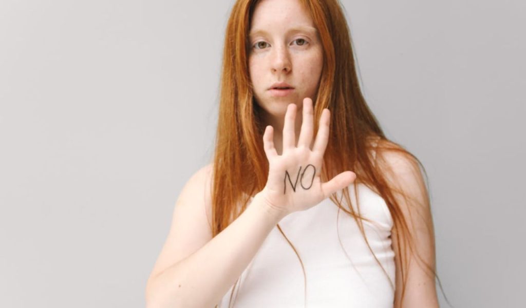 A person holding up a hand with “NO” written on the palm.