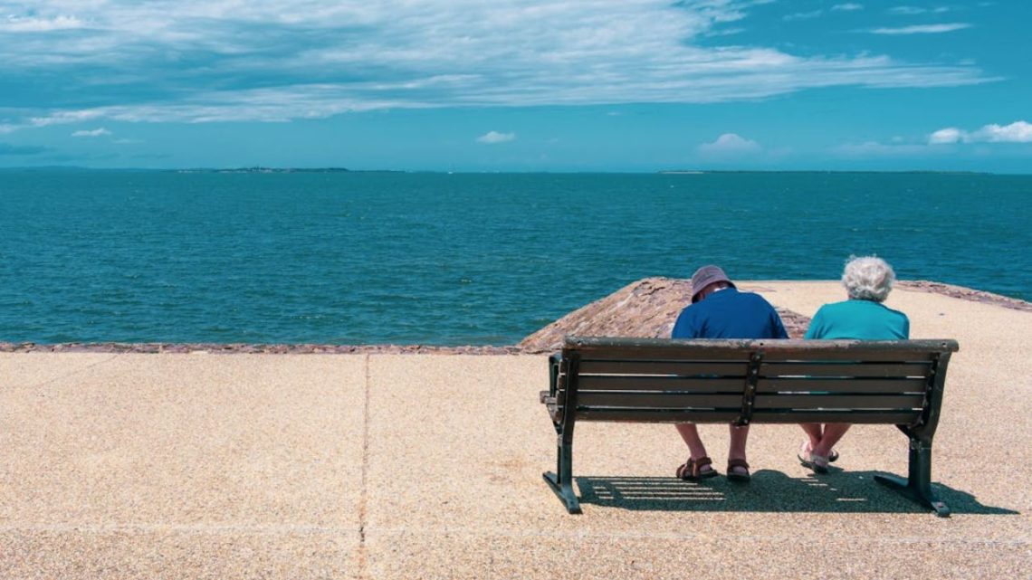 Two seniors on a bench facing the ocean.
