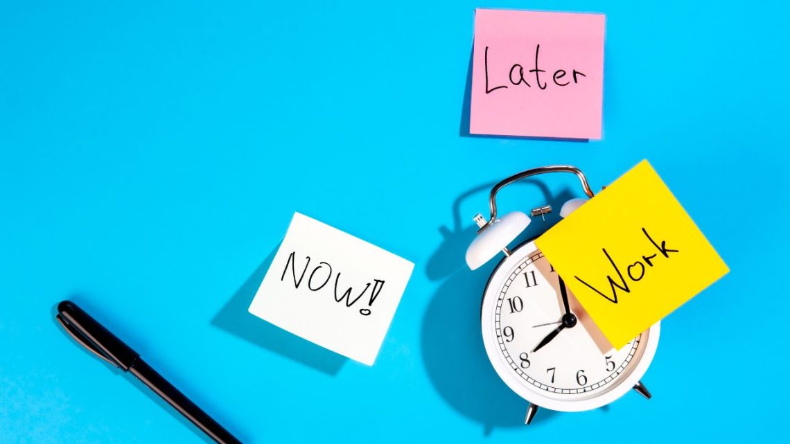 Alarm clock with sticky notes reading “Now,” “Later,” and “Work.”