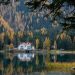 Quiet lake reflecting a white lodge with red roof, surrounded by dense pine forest and autumn trees.
