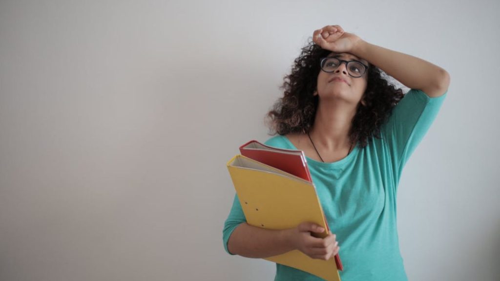 Stressed woman holding folders with her hand on her forehead.