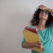 Stressed woman holding folders with her hand on her forehead.