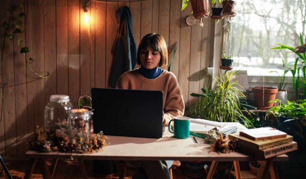 Person working on a laptop in a plant-filled room.