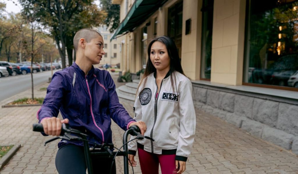 Two women talking on a sidewalk, one holding a bicycle.