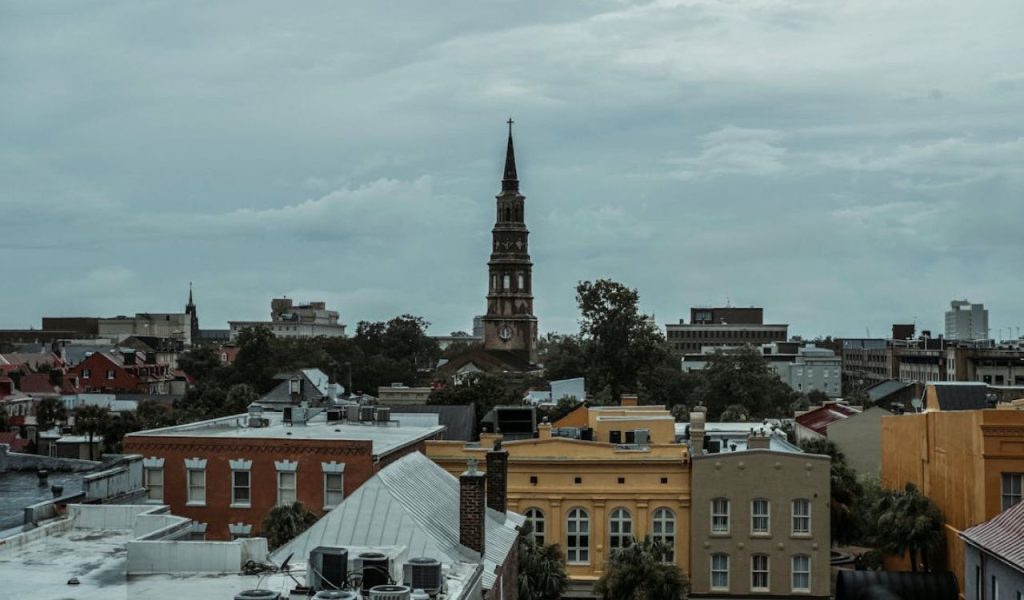 Charleston skyline with historic church steeple above low rooftops under cloudy skies.