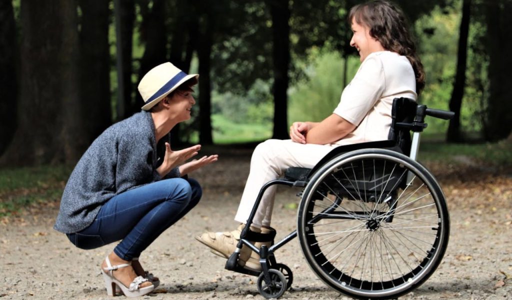 Woman talking with a person in a wheelchair outdoors.