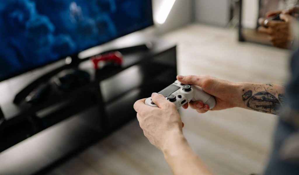 Hands holding a game controller in front of a TV.