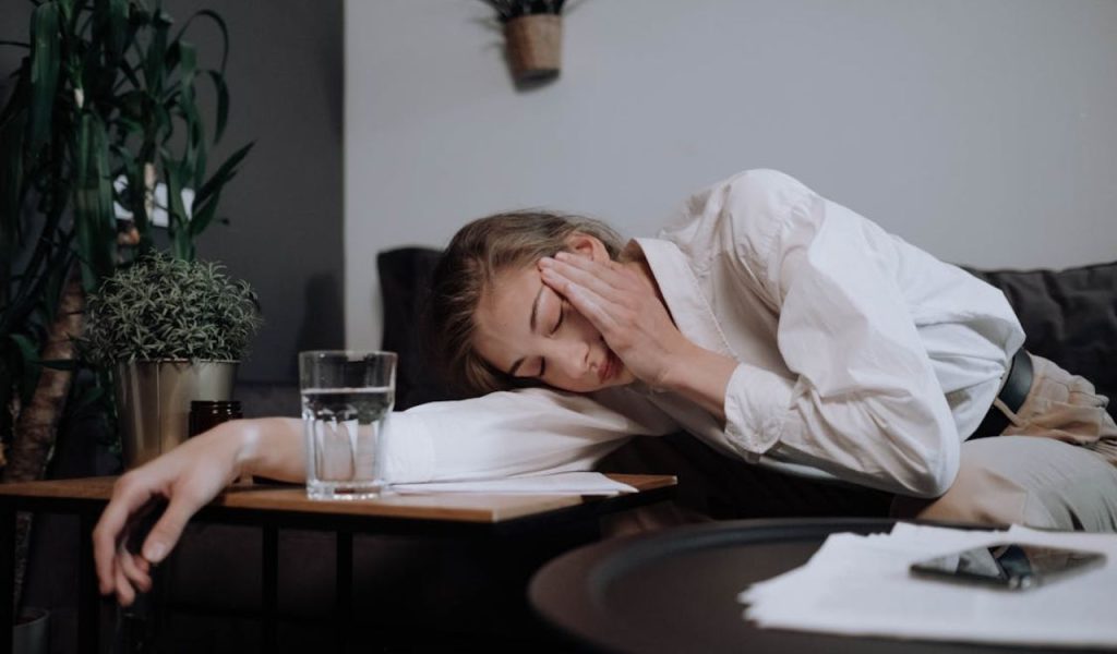 Tired woman resting her head on a table beside a glass of water.