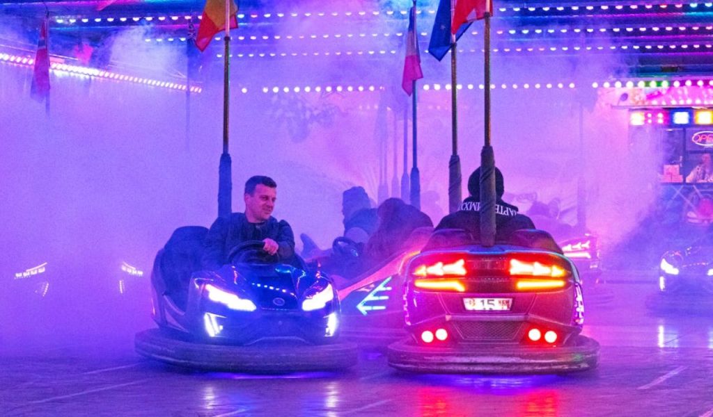 People riding bumper cars under colorful lights and fog.