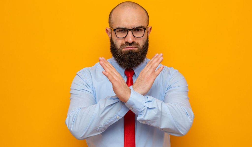 Man with crossed arms making a “no” gesture on a yellow background.