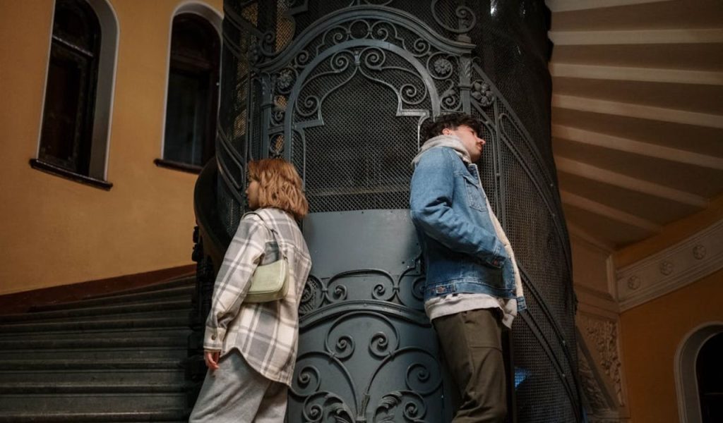 Two people standing back-to-back by an ornate gate.
