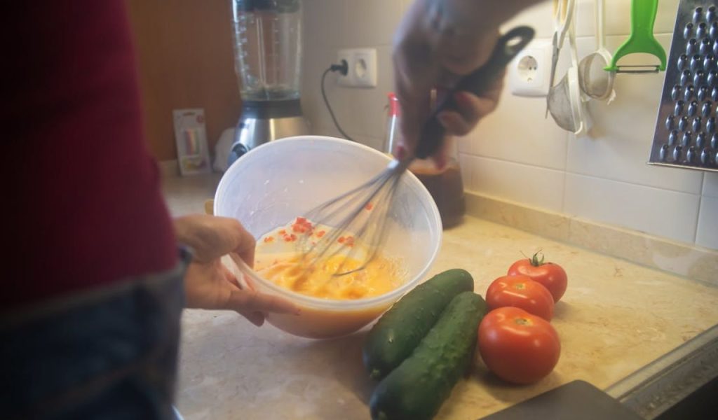 Person whisking eggs in a bowl on a kitchen counter.
