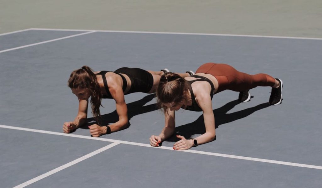 Two women doing plank exercises on an outdoor court.