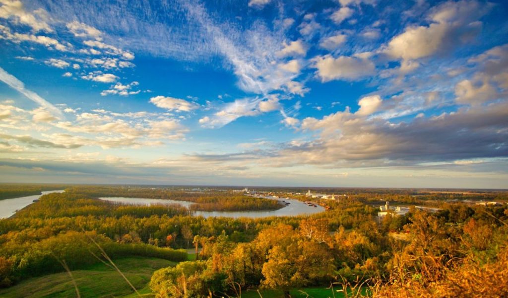Wide river and forest landscape under a dramatic blue sky.