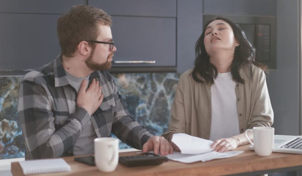 Two people discussing at a kitchen table with papers.