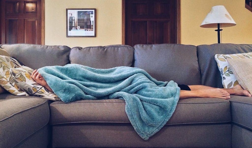 Person resting on a couch under a blanket.