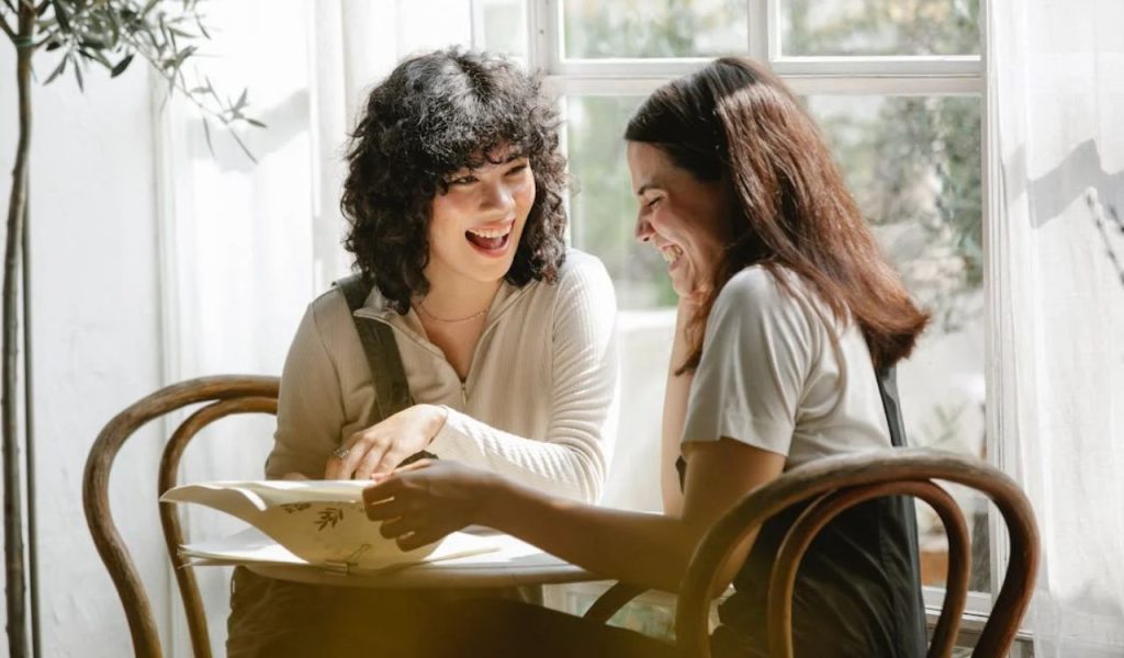 Two friends laughing together at a table.