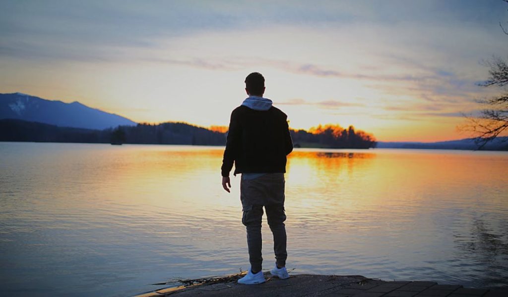 Person standing by a lake at sunset, looking at the horizon.