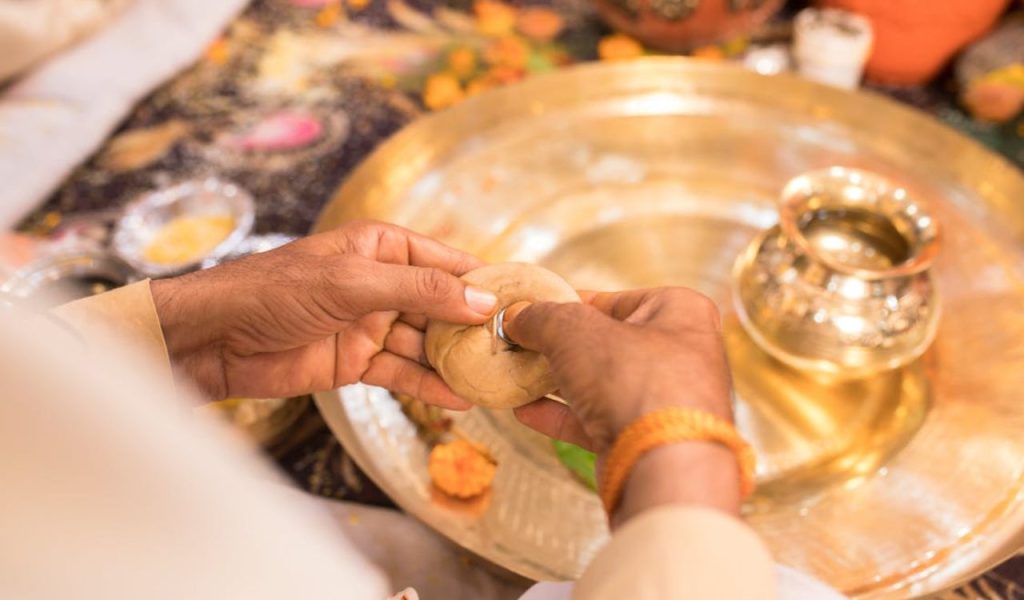 Hands holding a ring during a traditional ceremony with a brass tray.