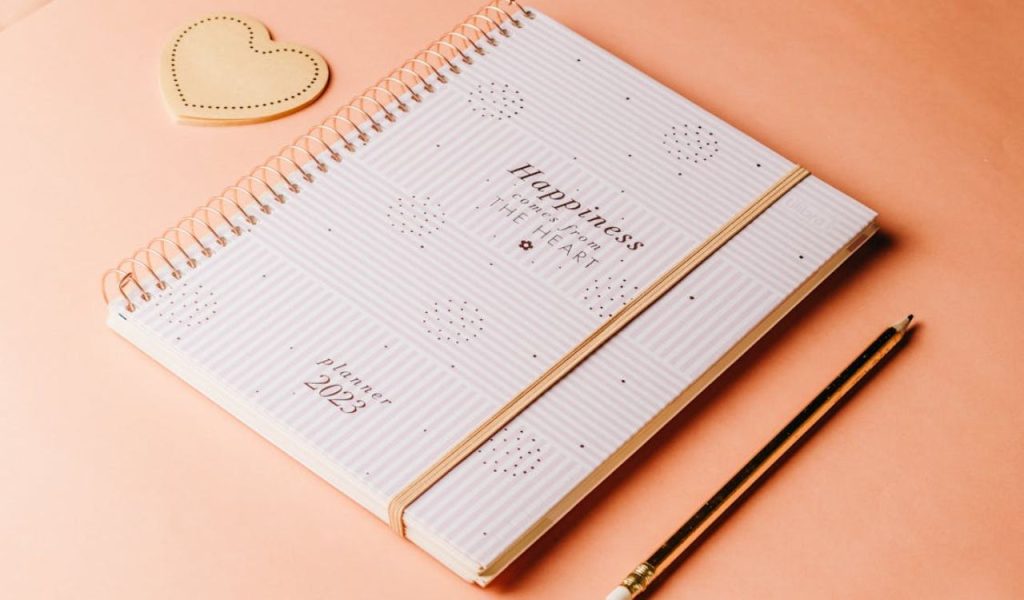 Spiral planner notebook with a pencil on a pink desk.
