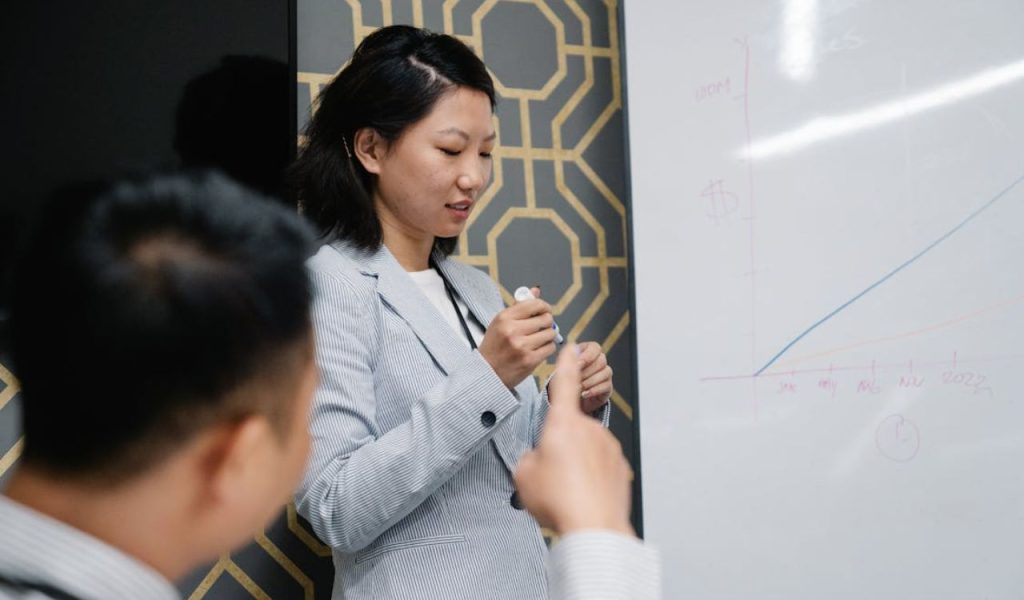Woman presenting at a whiteboard with a line graph.