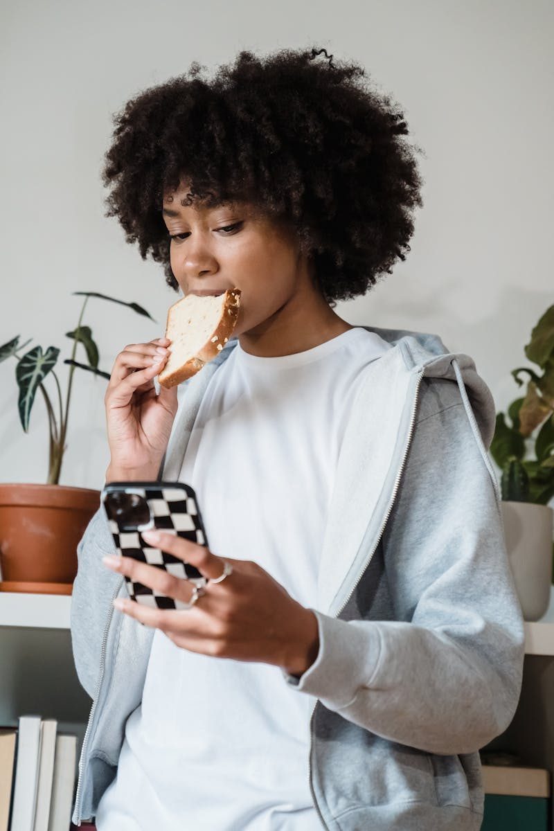 Casual indoor portrait of a woman enjoying bread and using her phone.