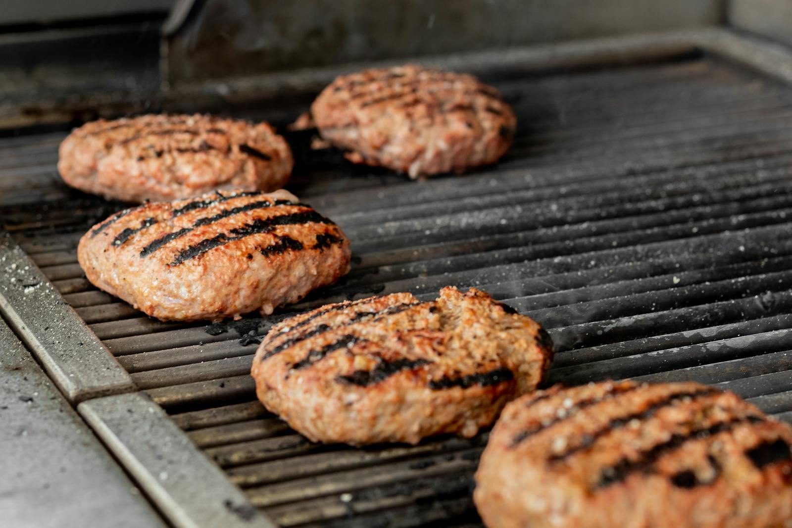 Close-up of sizzling beef patties cooking on a barbecue grill, showcasing grilling perfection.