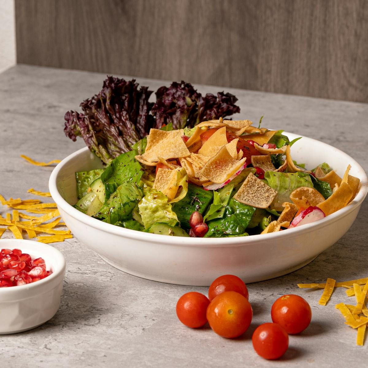A vibrant vegetable salad with cherry tomatoes, pomegranate seeds, and crunchy toppings in a white bowl.