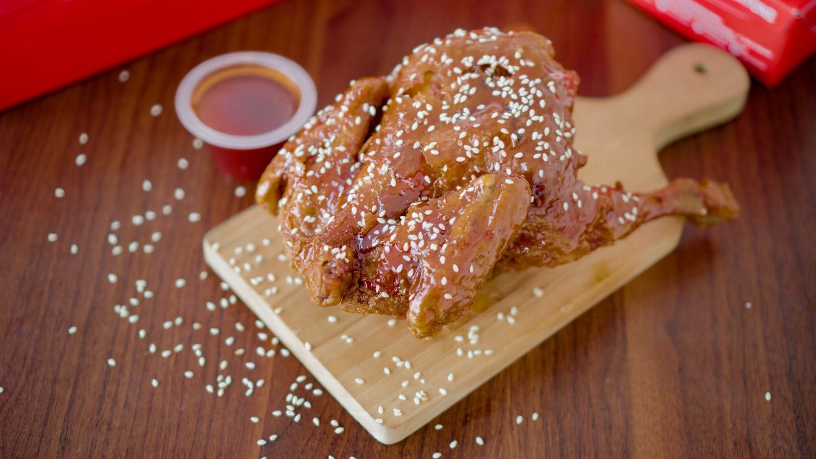 Delicious fried chicken topped with sesame seeds, served on a wooden board with sauce.