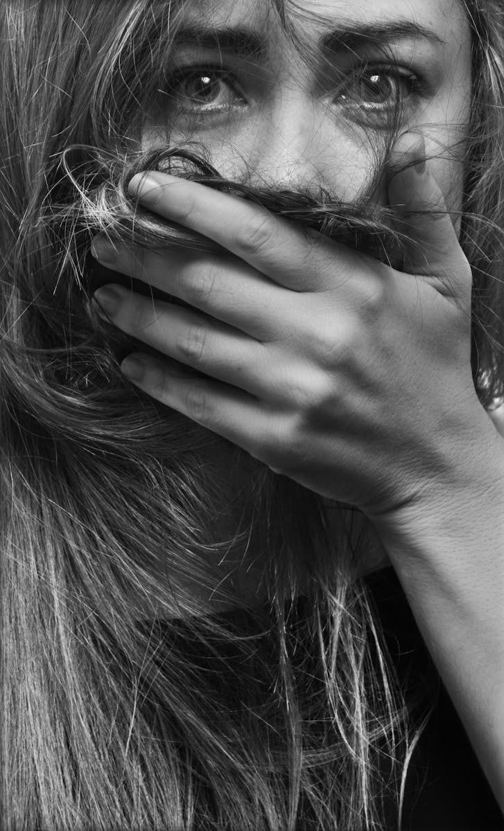 Dramatic close-up of a woman with hand covering mouth, expressing intense emotion.