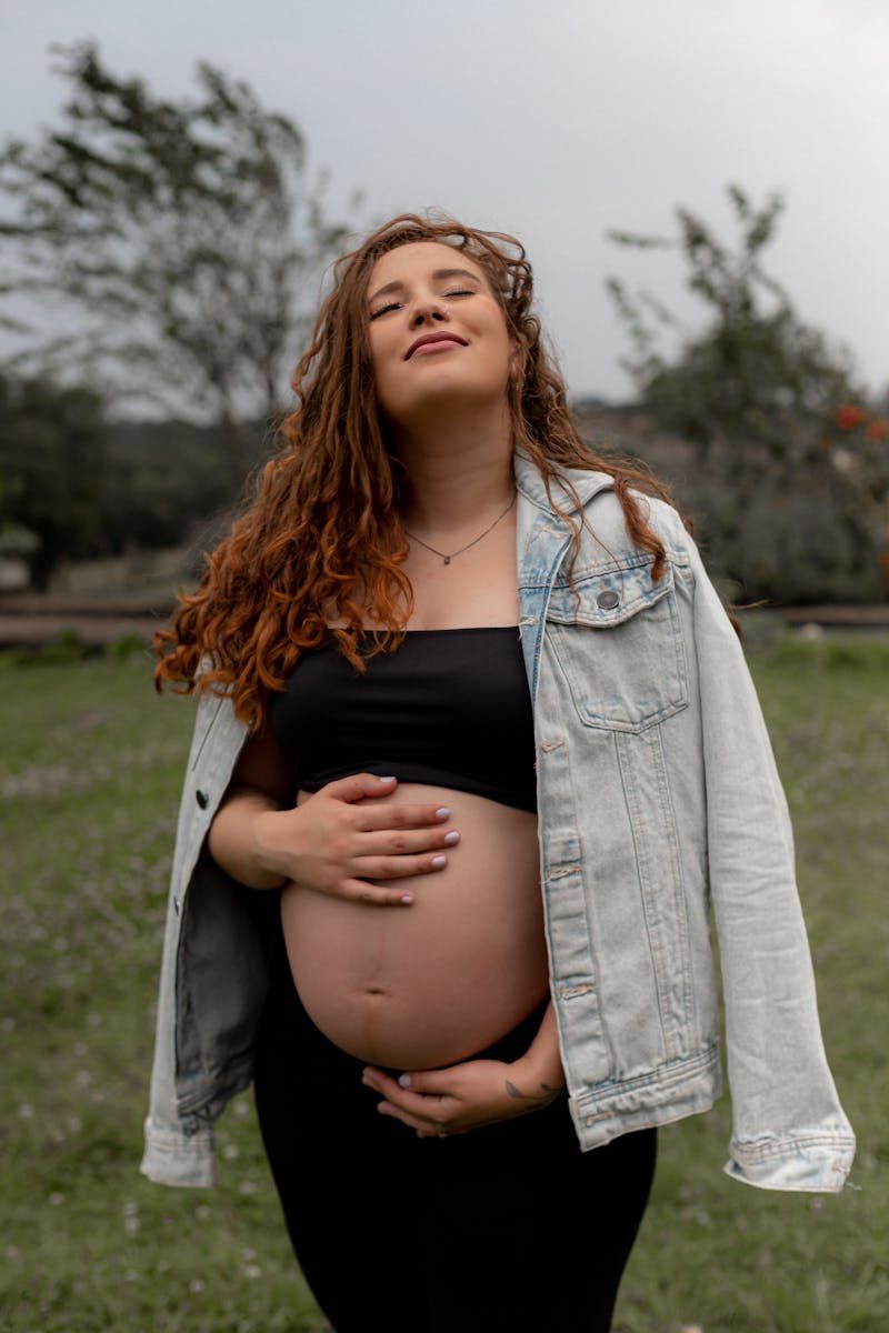 Pregnant woman smiling with eyes closed, touching belly outdoors, exuding happiness and tranquility.