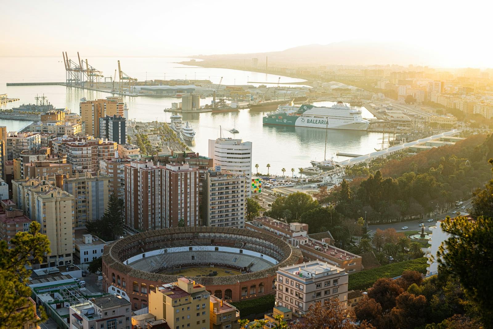 Stunning aerial shot of Malaga featuring the bullring and busy harbor at sunset.