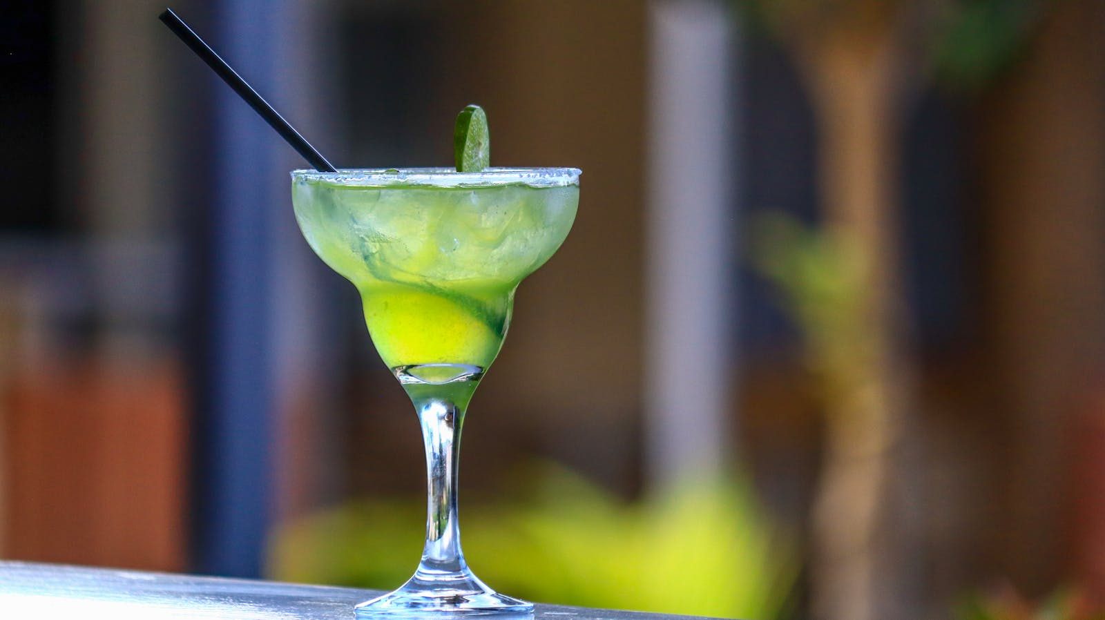 Close-up of a vibrant green margarita cocktail with a lime wedge in a glass.