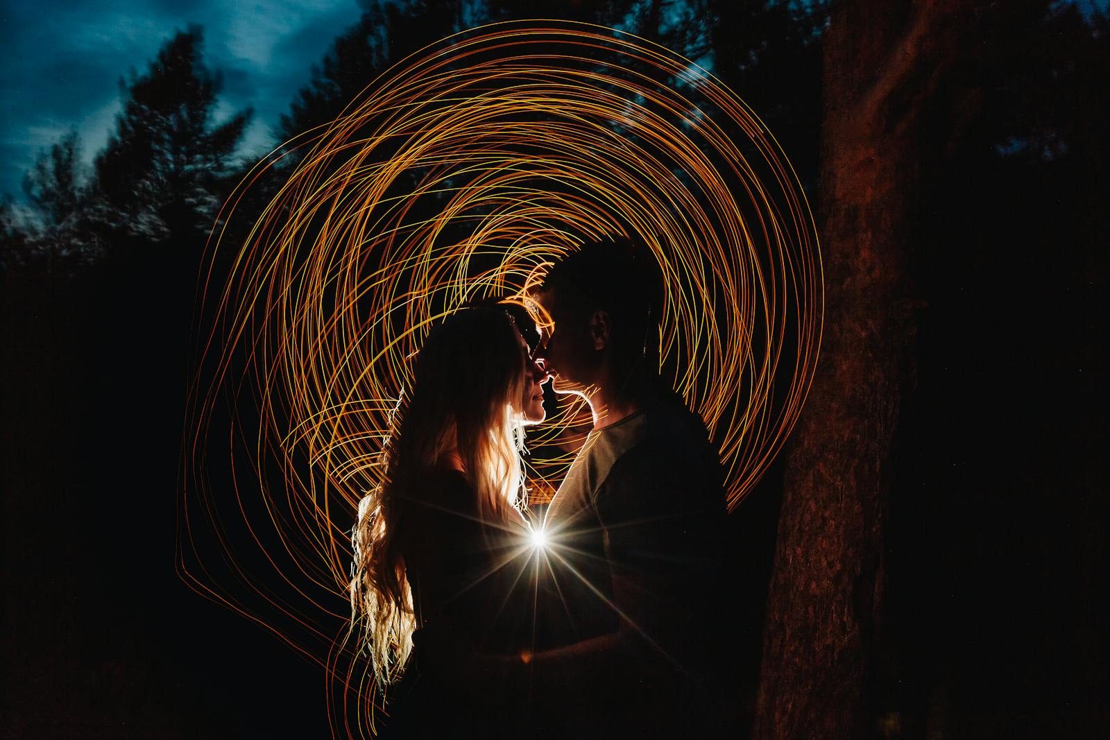 Silhouette of a romantic couple with artistic light painting effects in a nighttime forest setting.