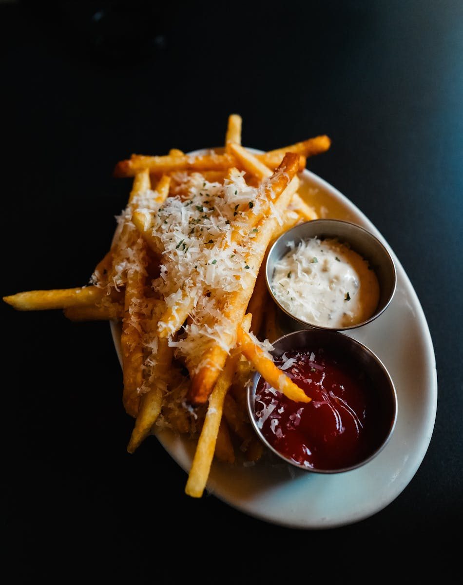 A plate of crispy parmesan truffle fries served with ketchup and mayo dip.