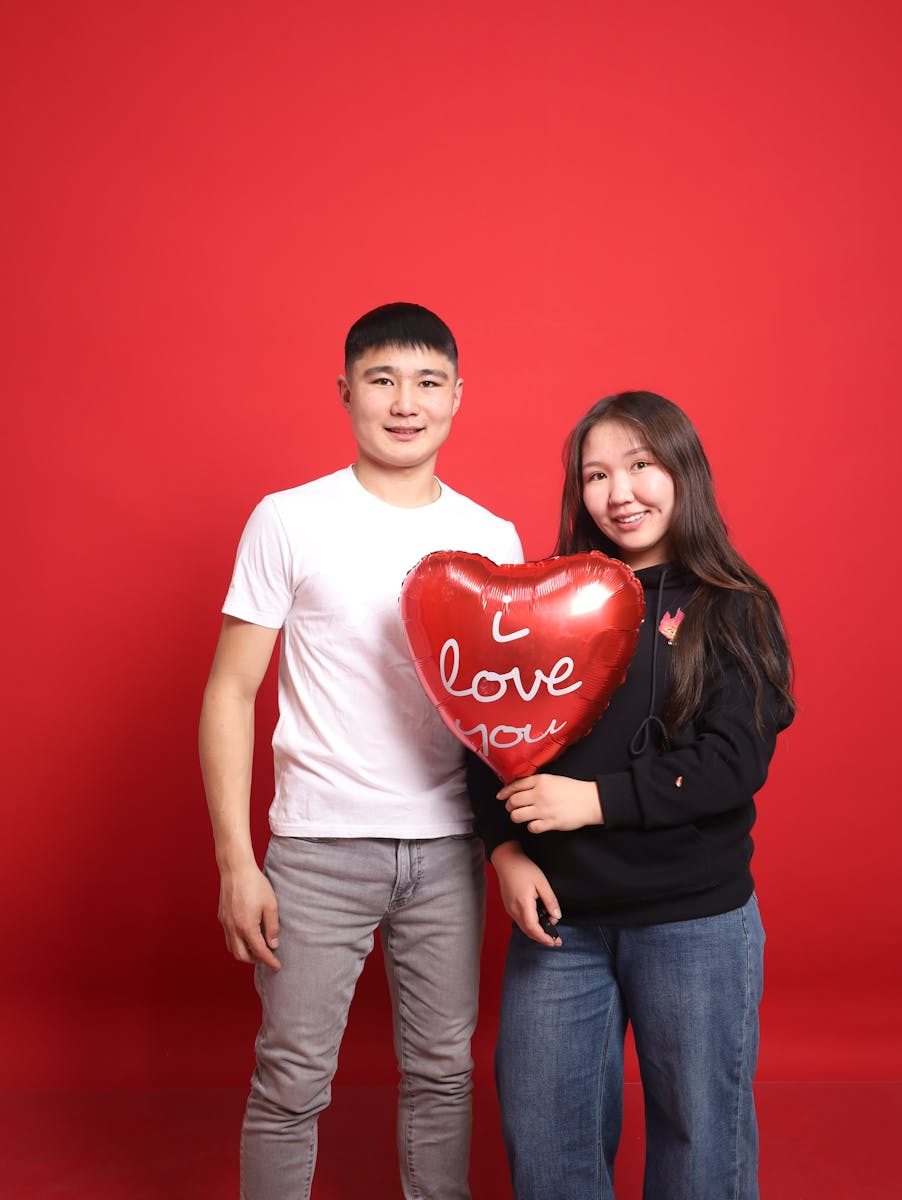 Couple holding a heart-shaped balloon saying 'I love you' against a red backdrop.