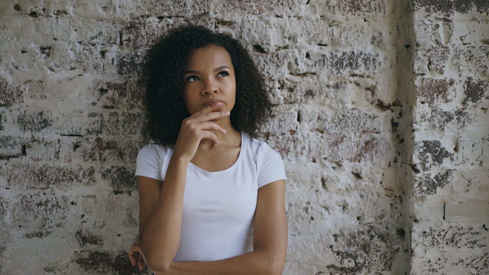 Teenage girl in deep thought leaning against a rustic brick wall.