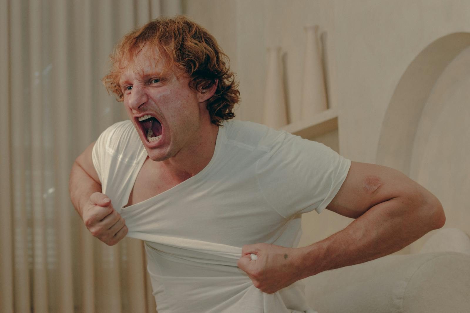 A man expressing intense emotion by tearing his white t-shirt indoors. Captured in São Paulo.