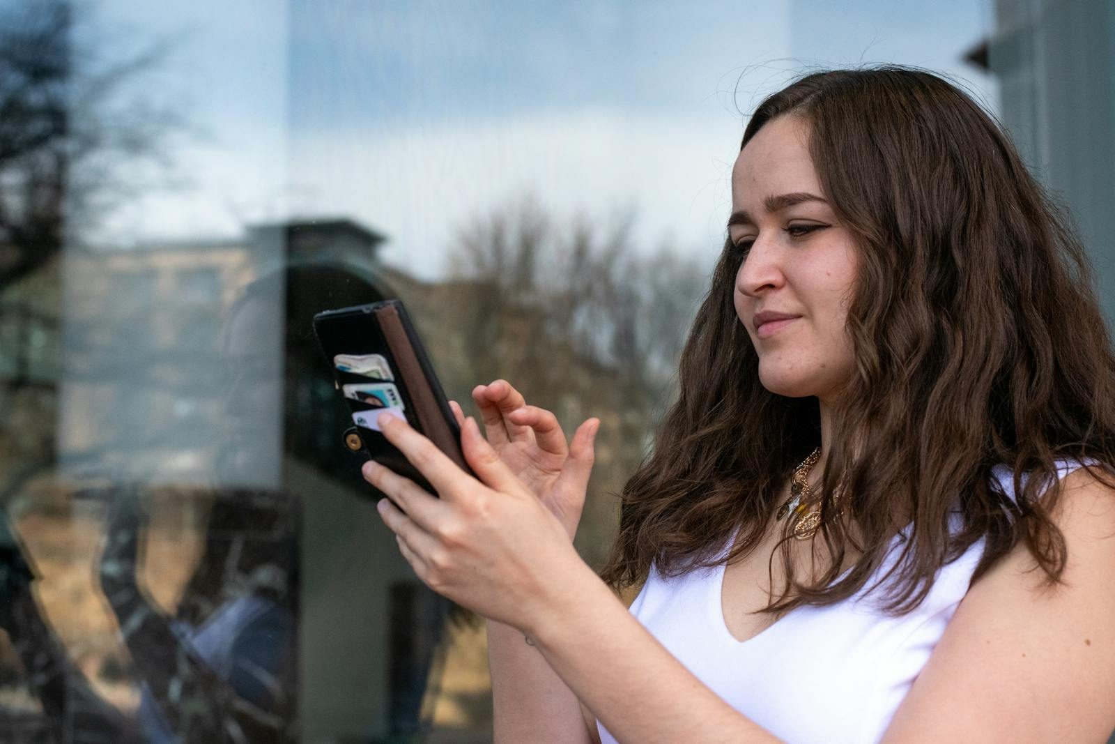 Young woman in a white dress using her smartphone outdoors. Bright day with reflections in a window.