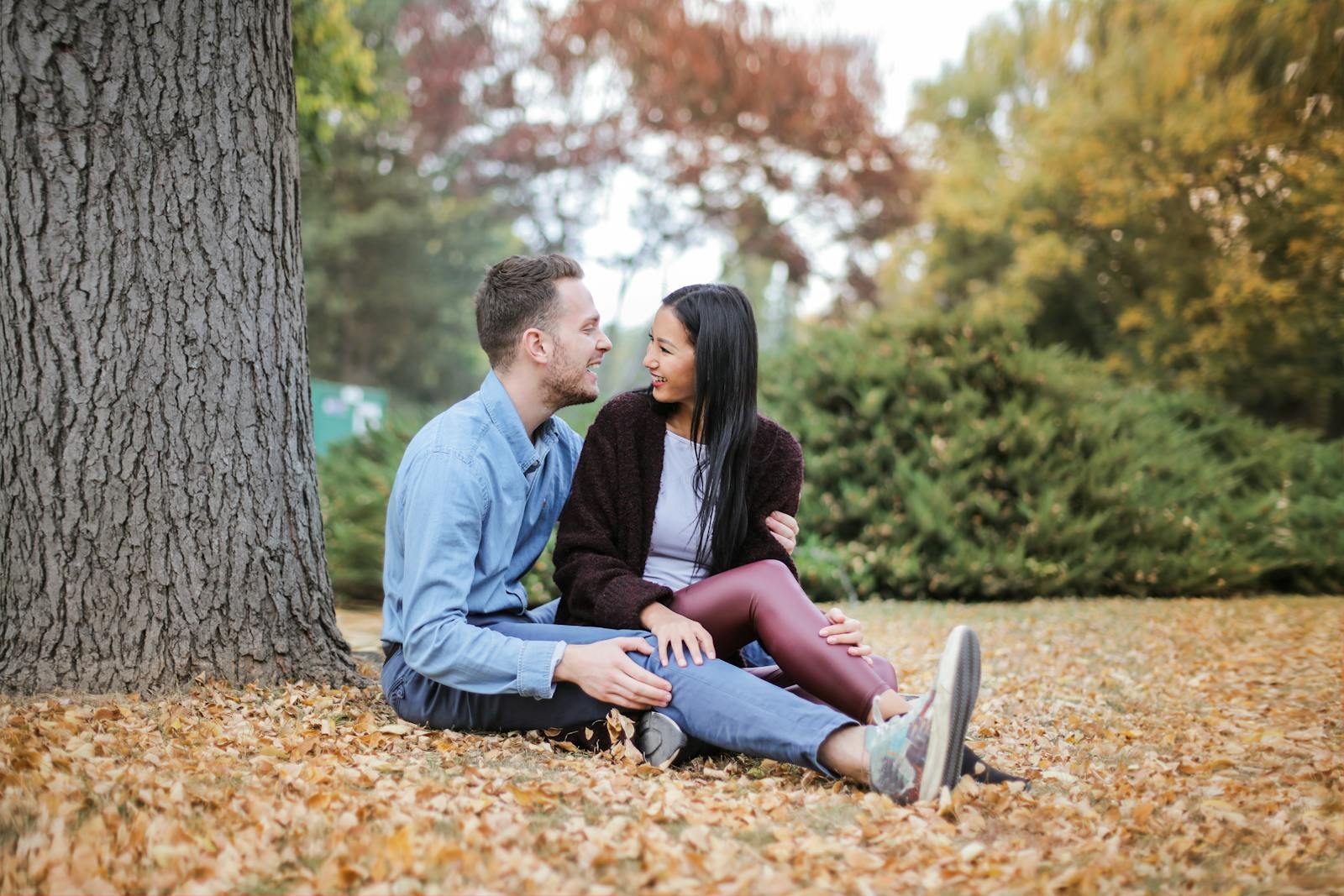 A joyful couple sitting on fallen leaves in a park, embracing love and happiness during autumn.