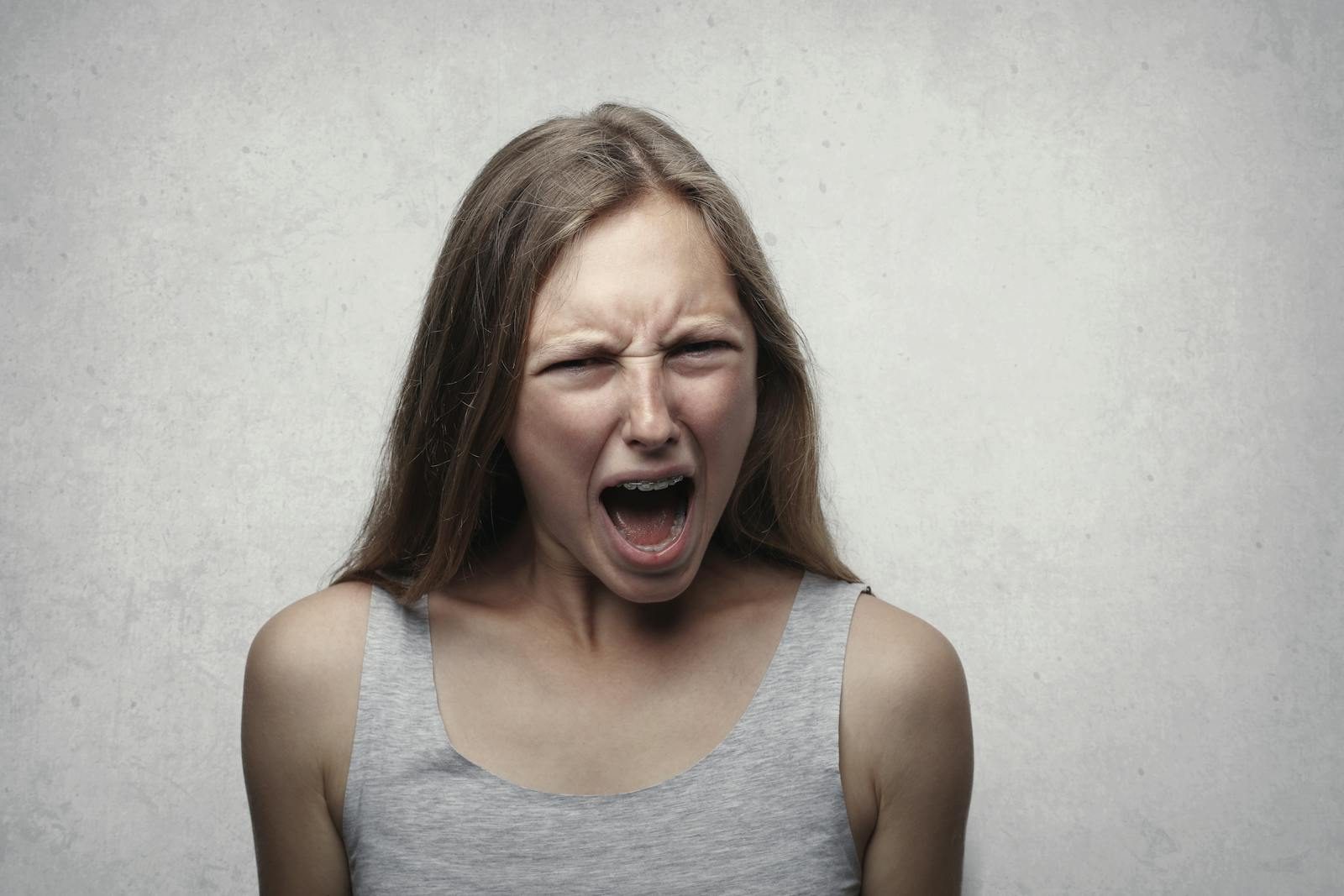 A woman with an intense facial expression screaming against a neutral gray background.
