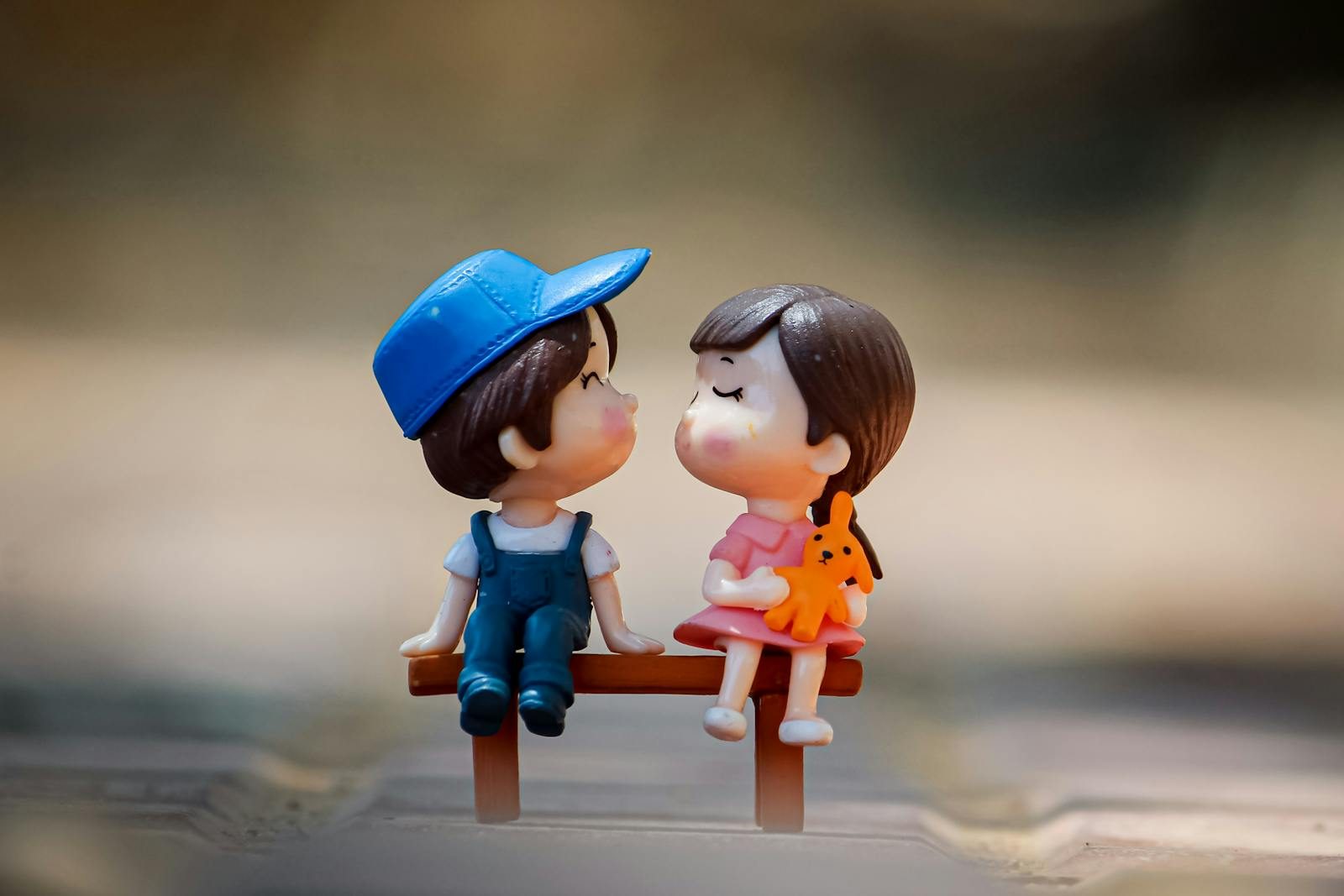 Tiny figurine of cute little girl and boy sitting on bench together and kissing