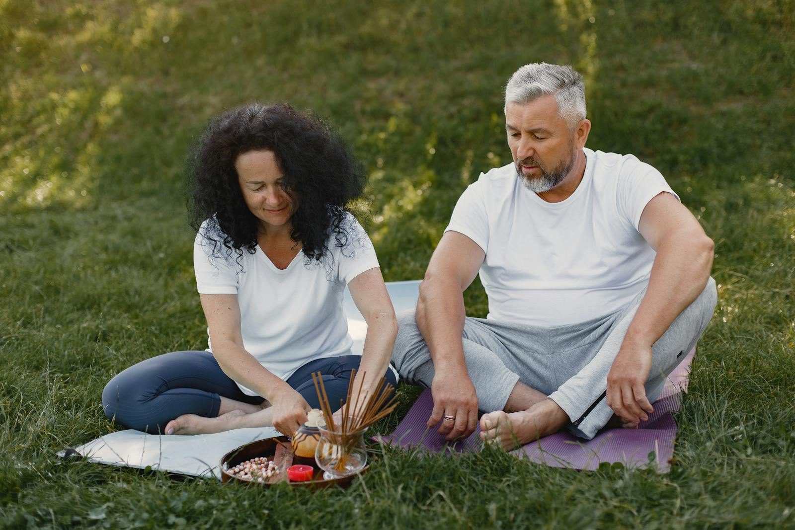 Elderly couple sitting on grass with incense sticks, enjoying a peaceful outdoor moment.