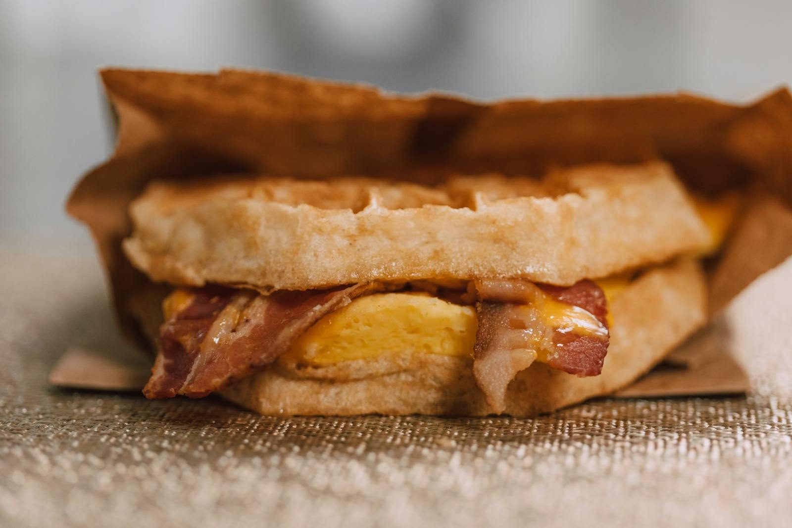 Mouthwatering waffle sandwich with bacon, egg, and cheese wrapped in paper.